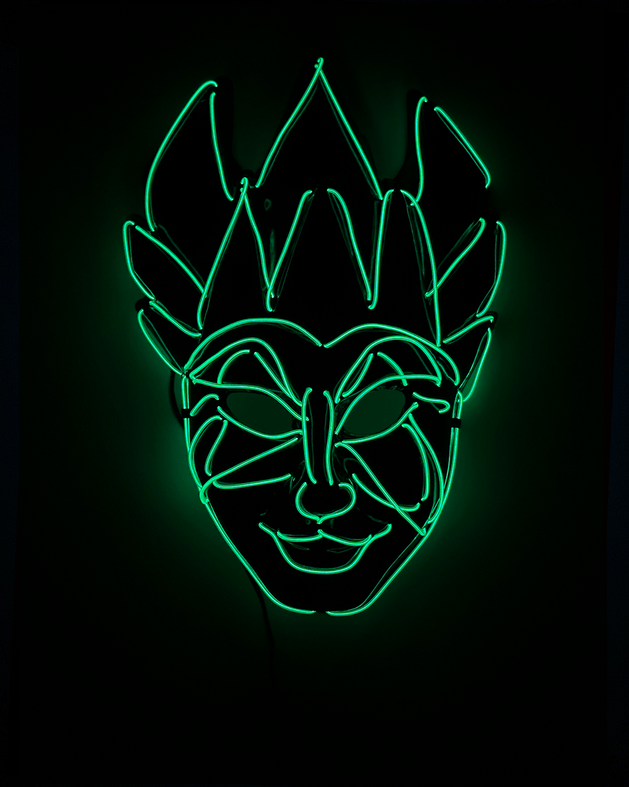 Bright green neon light outlines a mischievous mask with pointed ears and a wide smile on a black background.